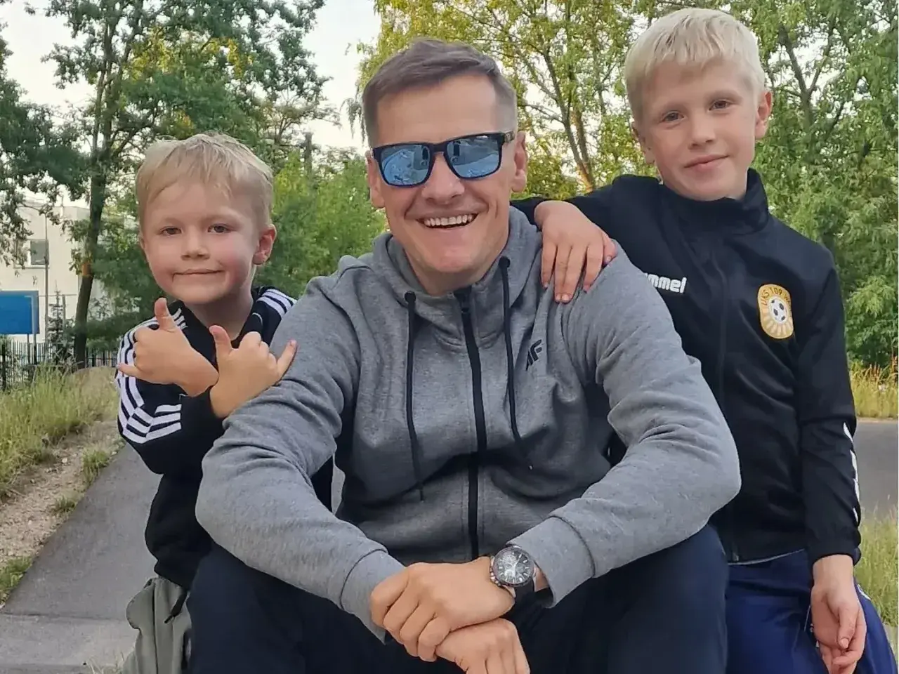 Marcin Mroczek z uśmiechem i dwoma synami, którzy przytulają się do niego.