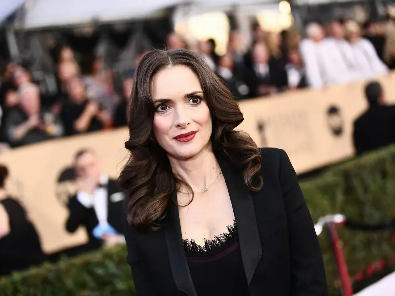 Winona Ryder w czarnej marynarce, z burzą brązowych włosów. Wygląda jakby opowiadała o swoich dzieciach.