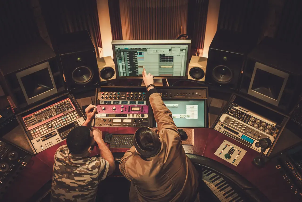 Dwóch producentów muzycznych w Polsce pracuje nad nowym hitem w studio nagraniowym, otoczeni sprzętem i monitorami.