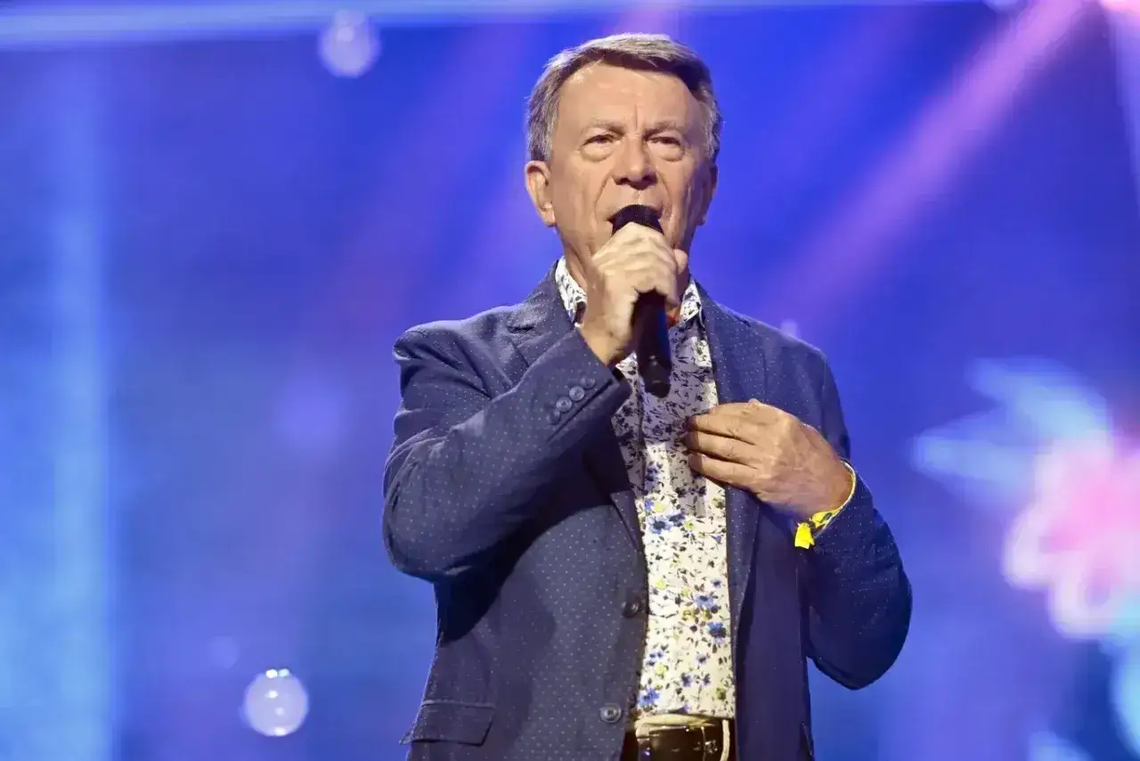 Wojciech Gąsowski śpiewa na scenie w niebieskiej marynarce w kropki i kwiecistej koszuli.