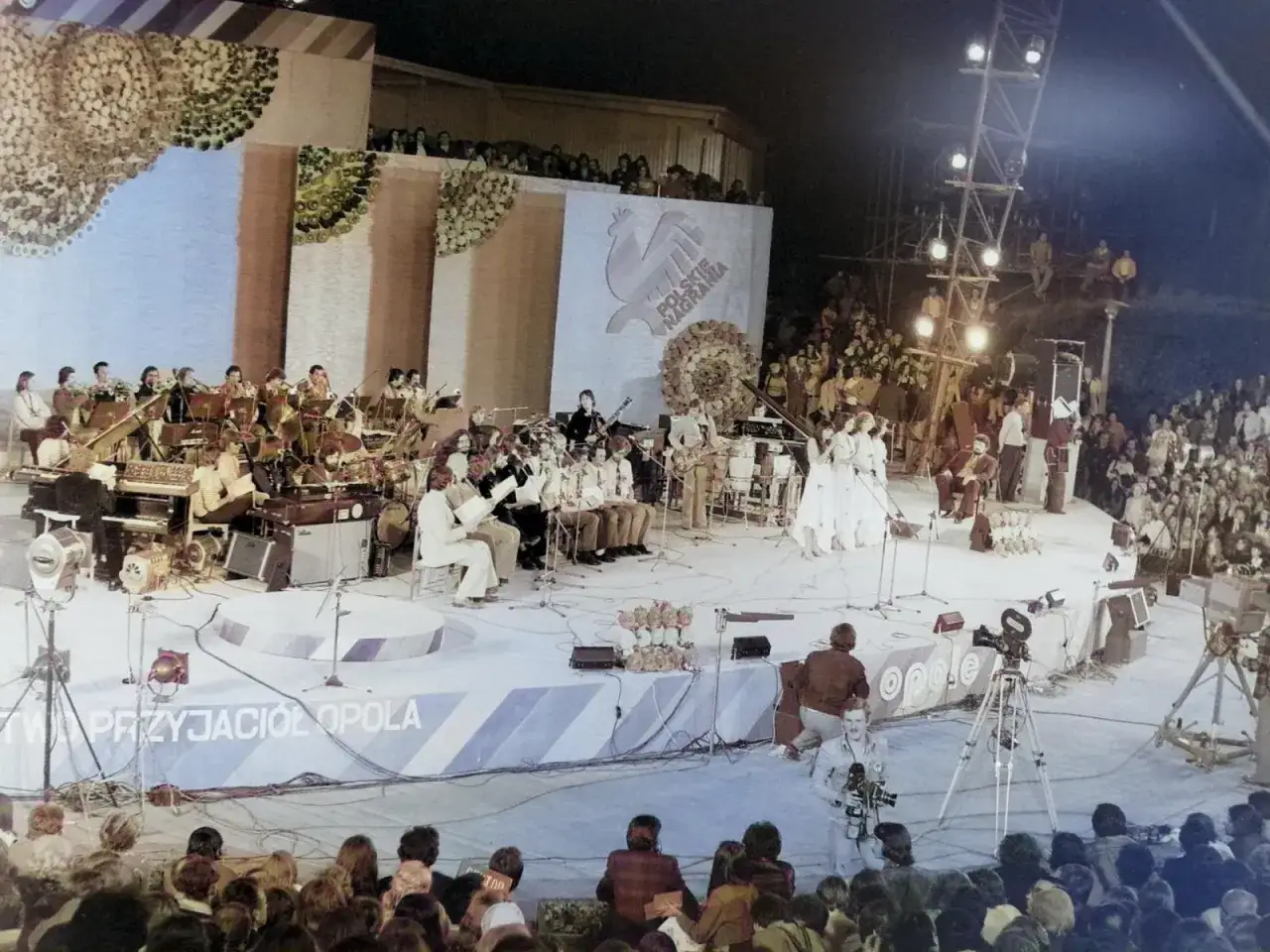 Wielka scena podczas festiwalu w Opolu. Orkiestra, wokaliści i tłumy widzów tworzą niezapomnianą atmosferę.