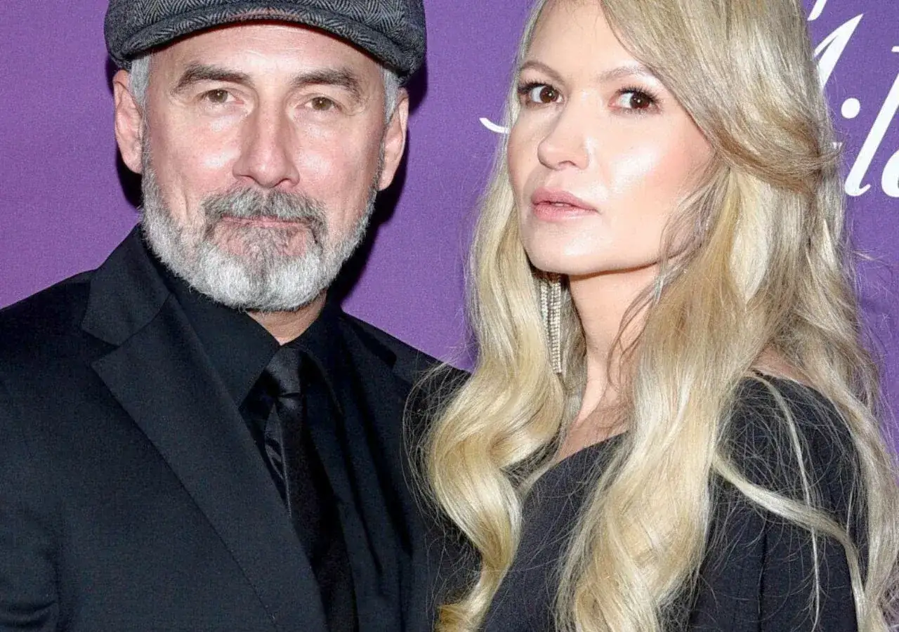 Jacek Kopczyński z żoną, elegancko ubrani, pozują do zdjęcia na fioletowym tle.