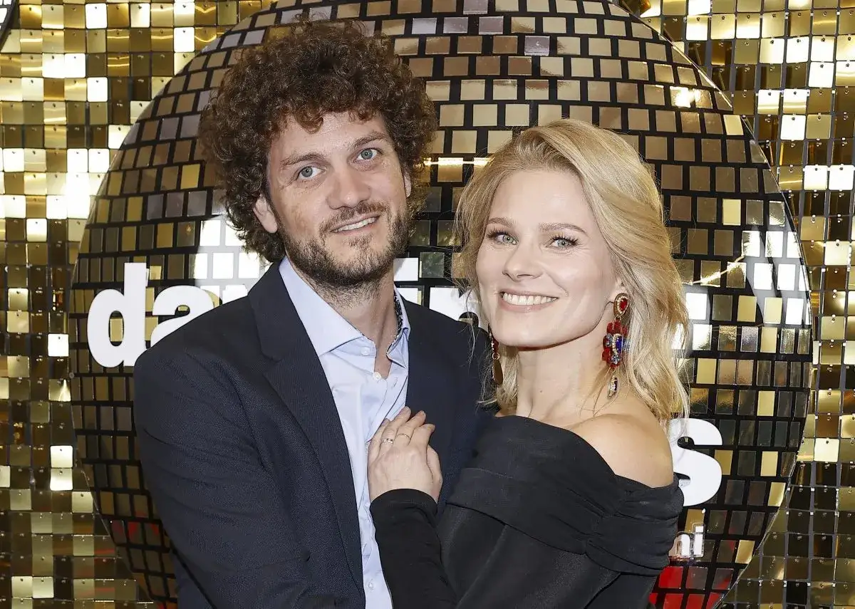 Anna Głogowska z partnerem pozują na tle złotej, lustrzanej ściany.